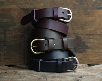 May include: A stack of four leather belts in different colors, including brown, dark brown, burgundy, and black. Each belt has a silver or gold buckle.