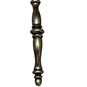 May include: An antique-style cabinet pull handle in brass. The handle has an ornate design with a warm, aged gold finish. The handle is vertically oriented. The cabinet handle is likely new.