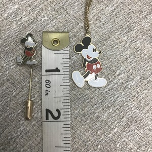 Puede incluir: Un conjunto de broche y collar de Mickey Mouse en tono dorado. El broche mide aproximadamente 2,5 cm de alto y el collar mide aproximadamente 45 cm de largo. Ambos presentan una imagen de dibujos animados de Mickey Mouse con sus caracter&iacute;sticos pantalones cortos rojos.