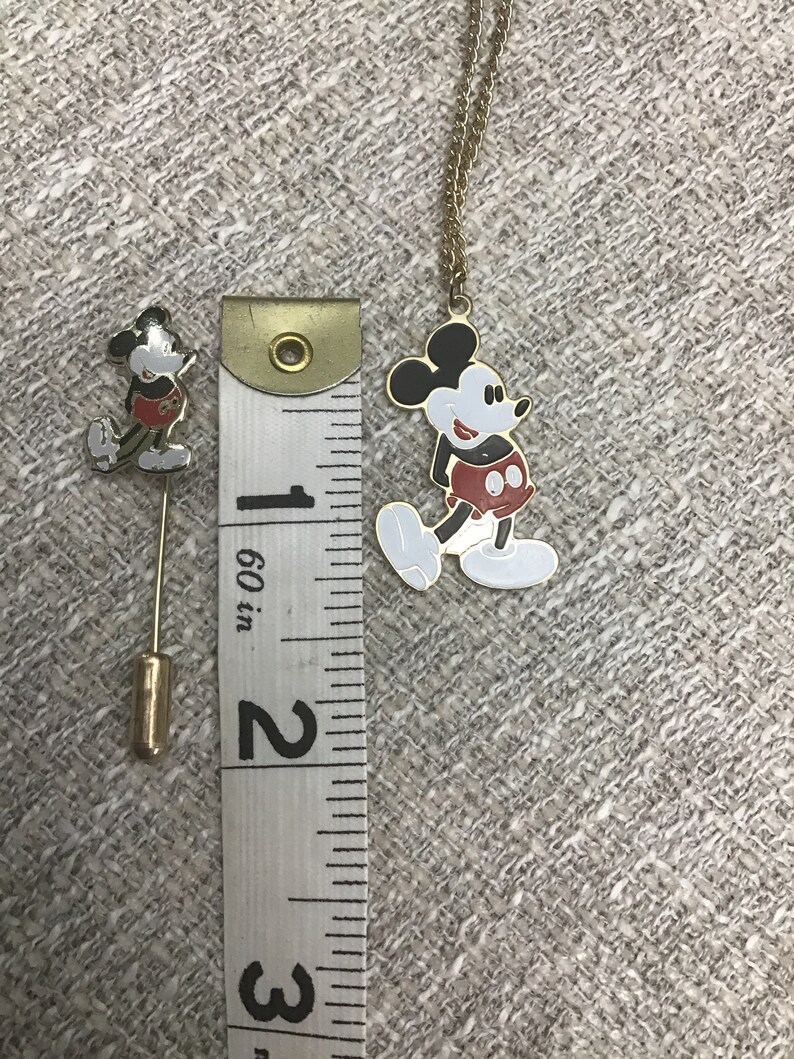 Puede incluir: Un conjunto de broche y collar de Mickey Mouse en tono dorado. El broche mide aproximadamente 2,5 cm de alto y el collar mide aproximadamente 45 cm de largo. Ambos presentan una imagen de dibujos animados de Mickey Mouse con sus caracter&iacute;sticos pantalones cortos rojos.