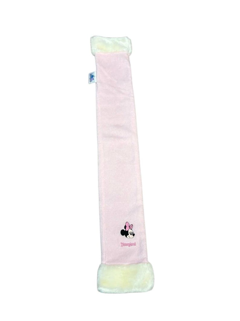 May include: A pale pink scarf with white faux fur edging. It has an embroidered Minnie Mouse motif and the word "Disneyland" in pink script.