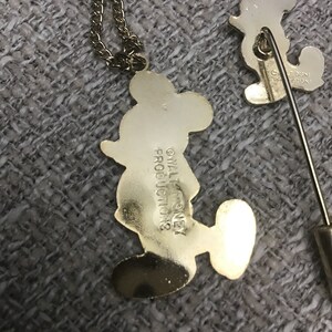 Puede incluir: Un conjunto de collar y broche de Mickey Mouse en tono dorado. El collar presenta un colgante de Mickey Mouse con el texto "&copy; WALT DISNEY PRODUCTIONS" en la parte posterior. El broche presenta un dise&ntilde;o de Mickey Mouse con el texto "&copy; WALT DISNEY PRODUCTIONS" en la parte posterior.