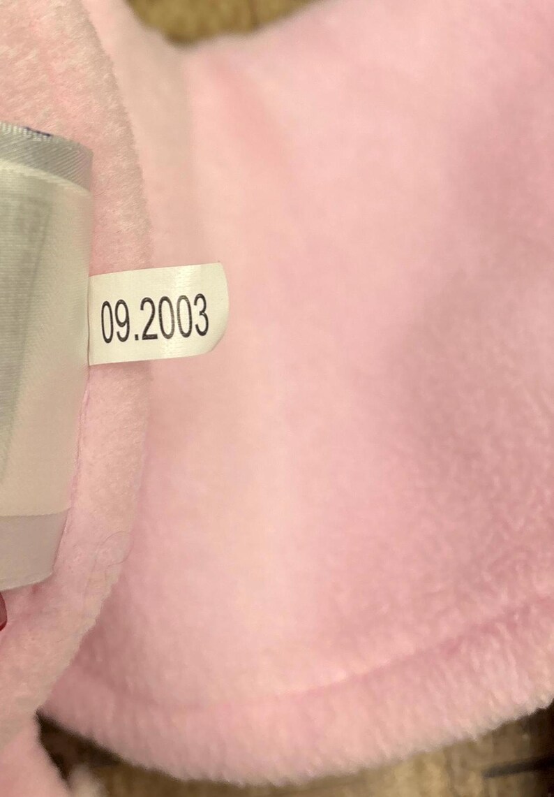 May include: A close-up of a soft, pink fabric with a tag attached. The tag displays the date "09.2003" in black text. The fabric appears to be plush and textured, with a light pink hue.