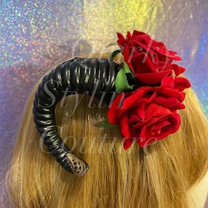 Könnte beinhalten: Schwarzer Haarklammer aus Kunst-Horn mit drei daran befestigten roten Rosen. Die Rosen sind aus Stoff und haben eine samtige Textur.