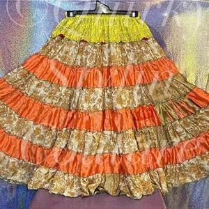 Peut inclure: Une longue jupe ample à plusieurs couches de tissu. La jupe est en tissu à motifs marrons et oranges avec une ceinture jaune.