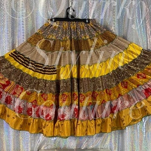 May include: A multi-layered skirt with a patchwork design. The skirt is made of various fabrics in shades of brown, yellow, red, and white. The skirt has a gathered waist and a flowing silhouette.