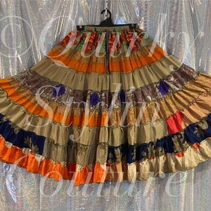 Può includere: Una gonna patchwork multicolore con una varietà di tessuti e motivi. La gonna è composta da diversi strati di tessuto, creando una silhouette ampia e fluida. La gonna è un mix vibrante di arancione, marrone, blu e rosso.