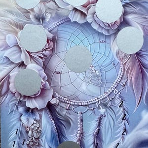 Könnte beinhalten: Karte mit einem Traumfänger-Design, mit sanften Blau-, Lila- und Rosatönen. Die Karte hat ein Blumen- und Federmotiv mit mehreren silbernen Rubbelkreisen. Der Text "Wünsche & Träume" steht oben.