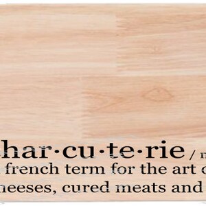 Puede incluir: Una tabla de cortar de madera con un mango. La tabla tiene la definición de "charcuterie" impresa: "char-cu-te-rie /sustantivo/ shar koo ter ee Un término francés para el arte de organizar fruta, quesos, carnes curadas y galletas"