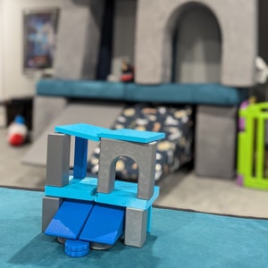 May include: A blue and gray toy block set with a bridge-like structure. The blocks are stacked on top of each other and have a variety of shapes and sizes.