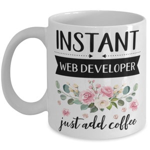 May include: White ceramic coffee mug with black text that reads "Instant Web Developer just add coffee". The text is surrounded by a floral design with pink and green flowers.