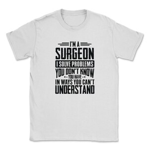 Puede incluir: Camiseta blanca con texto negro que dice "Soy un cirujano Resuelvo problemas que no sabes que tienes de maneras que no puedes entender."