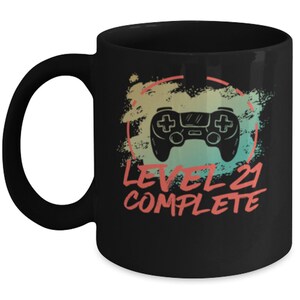 May include: Black coffee mug with a white design of a video game controller and the text "Level 21 Complete" in a vintage style.