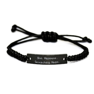 May include: Black braided bracelet with a black metal tag that reads "Shit Happens. Geocaching Helps."