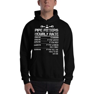 Op de afbeelding: Zwart hoodie met witte tekst die "PIPE FITTERS HOURLY RATE" luidt en een tabel met uurtarieven en beschrijvingen. De tarieven zijn € 100/uur, € 150/uur, € 175/uur, € 200/uur en € 250/uur.