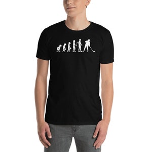 May include: Black t-shirt with a white graphic of the evolution of hockey. The graphic shows a series of stick figures, starting with a primitive human and ending with a hockey player.