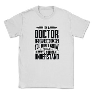 以下が含まれることがあります： 黒い文字で「私は医者です。私はあなたが知らない問題を、あなたが理解できない方法で解決します。」と書かれた白いTシャツです。