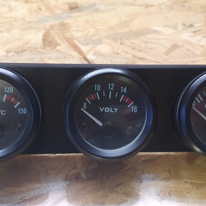 Puede incluir: Un panel negro con tres indicadores redondos. Los indicadores tienen caras blancas con agujas negras y marcas rojas. Los indicadores leen "OIL/°C", "VOLT" y "OIL/KG".