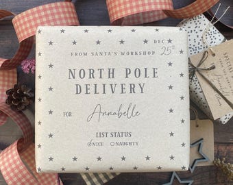 May include: A wrapped gift with a star pattern and the text "North Pole Delivery" for Annabelle. The gift is decorated with pink and white checkered ribbon and a tag that says "Special Delivery From The North Pole".