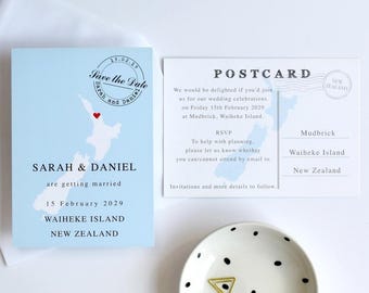 May include: A light blue Save the Date card featuring a map of New Zealand with a red heart, the text Sarah & Daniel are getting married 15 February 2029, and a matching white postcard with wedding details and a small white polka dot dish.