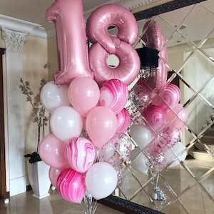 Może przedstawiać: Bukiet różowych i białych balonów z dużymi różowymi foliowymi cyframi 18. Balony są ułożone w grupie i związane srebrną wstążką.