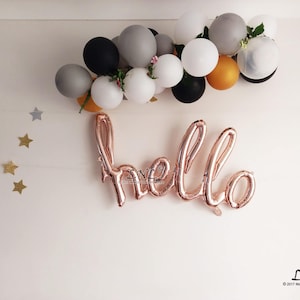 May include: A rose gold foil balloon spelling "hello" against a white background with a garland of grey, white, and gold balloons.