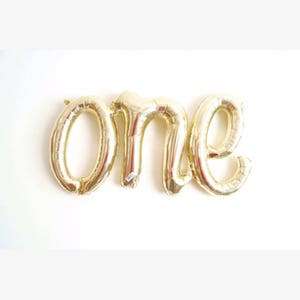 Könnte beinhalten: Goldene Folienballonbuchstaben, die das Wort "one" buchstabieren.