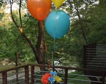 May include: A red octopus-shaped centerpiece with three balloons tied to it. The balloons are yellow, orange, and blue. The centerpiece is on a white table with a blue and white polka dot tablecloth.