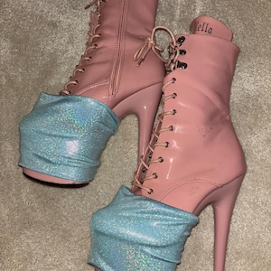 May include: A pair of pink platform boots with blue glitter boot cuffs. The boots have laces and a zipper on the back. The brand name "Pleaser" is visible on the side of one boot.