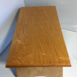 Puede incluir: Un taburete de madera con un acabado de madera natural. La parte superior del taburete es lisa y tiene un borde redondeado.