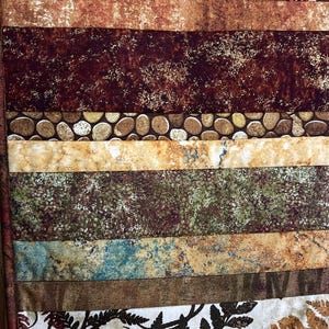 May include: A quilt with a brown, green and white patchwork design. The quilt is made of multiple layers of fabric and is quilted with a poly batting. The quilt is 12 1/2 inches by 45 1/2 inches.