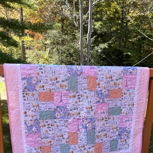 以下が含まれることがあります： ピンクと白のパッチワークキルトで、パリのテーマです。キルトには、自転車、木、エッフェル塔の画像が描かれています。キルトは、花柄や無地など、さまざまな生地で作られています。