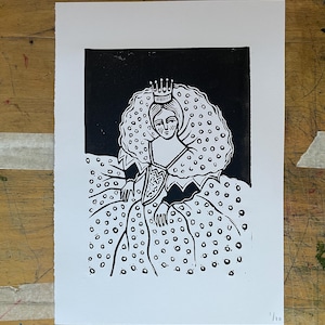May include: A black and white linocut print depicting a crowned figure with a large, dotted collar and patterned dress. The seated figure has clasped hands. The print is on white paper, with the edition number 1/10 visible.