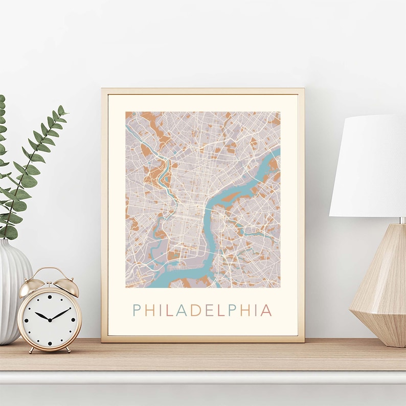 May include: A framed print of a map of Philadelphia, Pennsylvania. The map is in shades of brown, blue, and gray. The city name is printed in a colorful font at the bottom of the map.