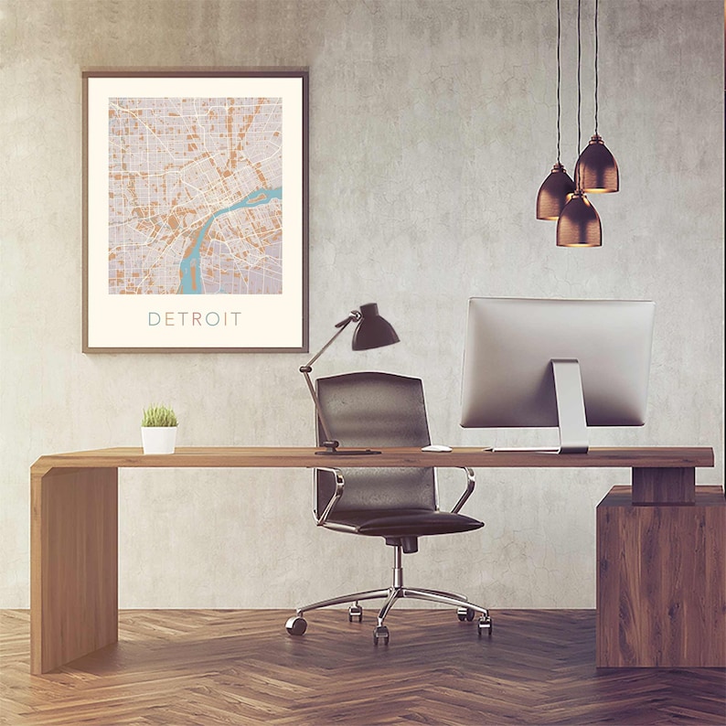 May include: A modern office workspace with a wooden desk, a black office chair, a computer monitor, a desk lamp, and a framed map of Detroit.