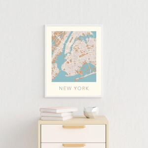 K&ouml;nnte beinhalten: Ein gerahmter Druck einer Karte von New York City mit hellblauem Hintergrund und braunen Linien. Der Text "NEW YORK" ist unter der Karte gedruckt.