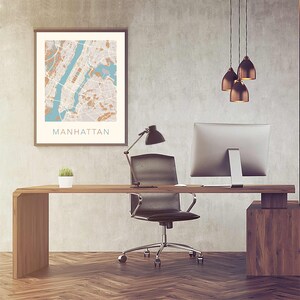 May include: A modern home office with a wooden desk, a black office chair, a computer monitor, a desk lamp, and a framed map of Manhattan.