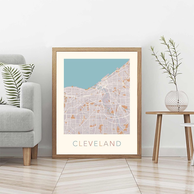 May include: A framed print of a map of Cleveland, Ohio. The map is in shades of blue, pink, and white, with the city's streets and waterways outlined in white. The word "CLEVELAND" is printed in pink, blue, and white at the bottom of the map.