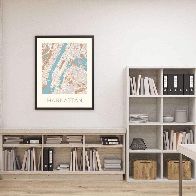 May include: A framed map of Manhattan, New York City, with a light brown and blue color scheme. The map is hanging on a white wall above a wooden bookshelf filled with books and decorative items.