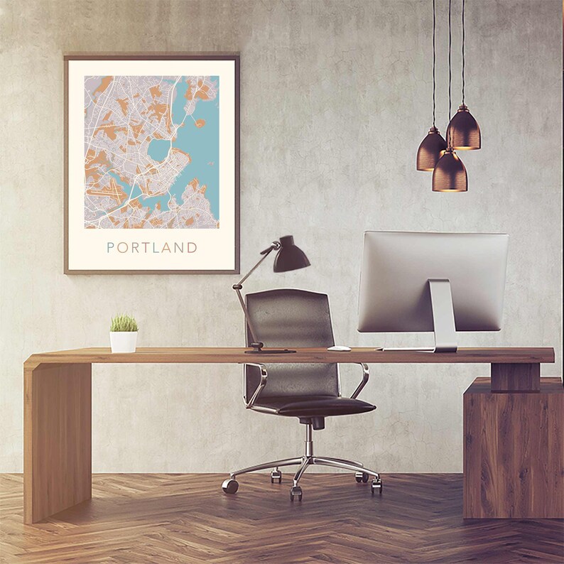 Pu&ograve; includere: Un ufficio domestico moderno con una scrivania in legno, una sedia da ufficio nera, un monitor per computer, una lampada da scrivania e una mappa incorniciata di Portland, Maine. Il muro &egrave; in cemento grigio chiaro.
