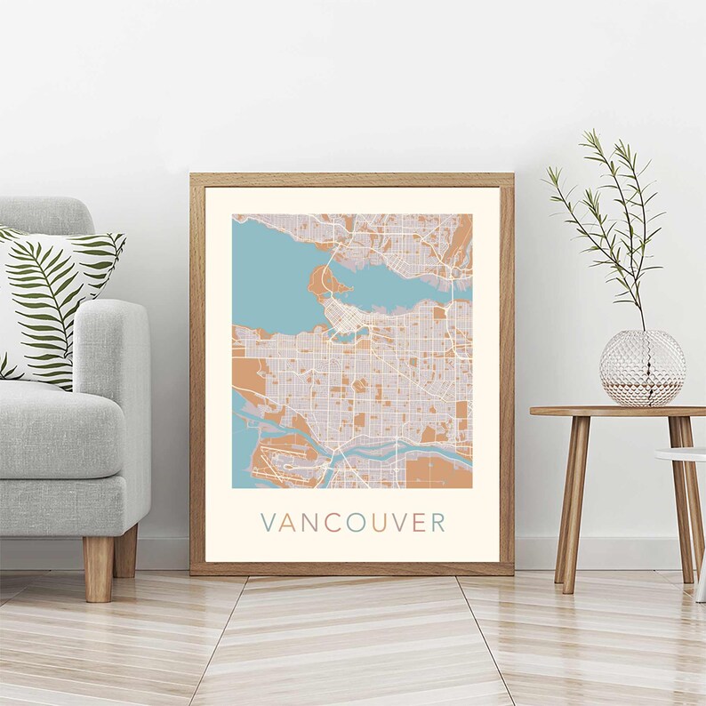 Op de afbeelding: Een ingelijste kaartprint van Vancouver, met een gedetailleerde stadsplattegrond in tinten beige, teal en bruin. Het woord "VANCOUVER" is in bijpassende teal kleur onderaan de print gedrukt. De print wordt weergegeven in een lichtbruine houten lijst.