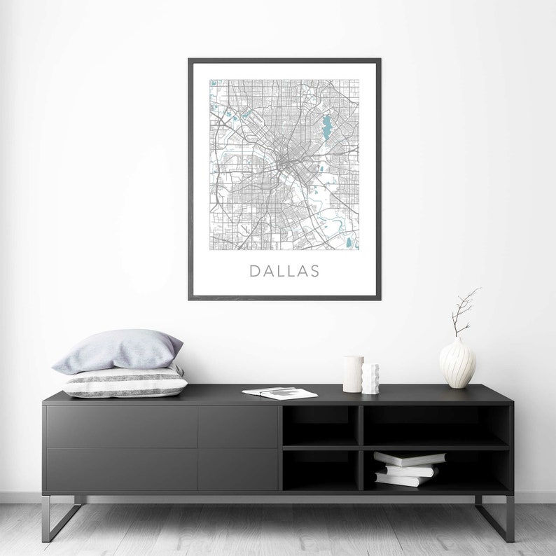 Pu&ograve; includere: Una stampa di mappa di Dallas, Texas in bianco e nero in una cornice nera appesa a una parete bianca sopra una consolle multimediale nera con due cassetti e tre ripiani. La consolle ha un cuscino bianco e due candele bianche in cima.