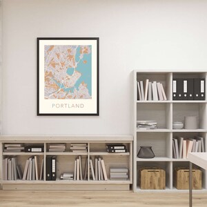 Pu&ograve; includere: Una mappa incorniciata di Portland, Maine, con uno schema di colori blu chiaro e arancione. La mappa &egrave; appesa a un muro bianco sopra una libreria in legno piena di libri e raccoglitori.