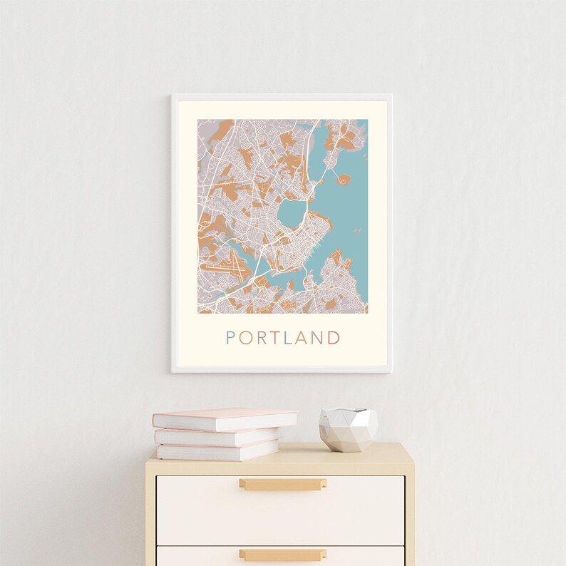 Pu&ograve; includere: Una stampa di mappa incorniciata di Portland, Maine, con uno schema di colori blu chiaro e beige. La mappa &egrave; esposta su una parete bianca sopra una cassettiera beige chiaro con maniglie dorate. Ci sono tre libri impilati sopra la cassettiera.