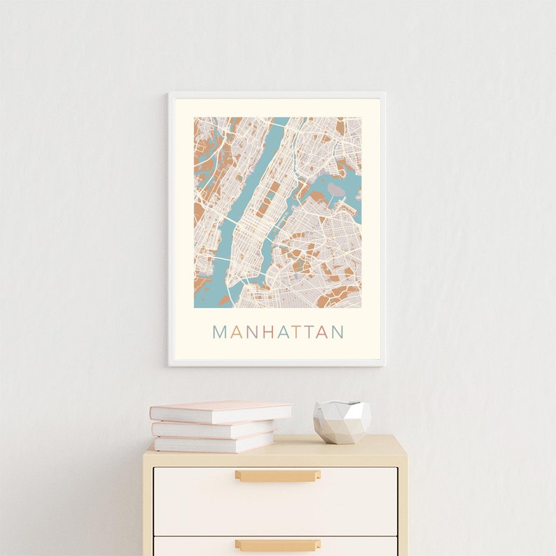 May include: A framed print of a map of Manhattan, New York City. The map is in shades of brown and blue, with the city streets and landmarks outlined in white. The word "MANHATTAN" is printed in a colorful font below the map.