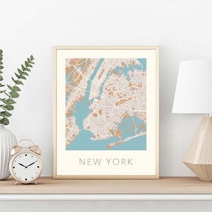 K&ouml;nnte beinhalten: Ein gerahmter Druck einer Karte von New York City mit hellblauem Hintergrund und braunen Linien, die die Stra&szlig;en darstellen. Der Text "NEW YORK" ist unter der Karte in hellrosa, hellblau und hellbraun gedruckt.
