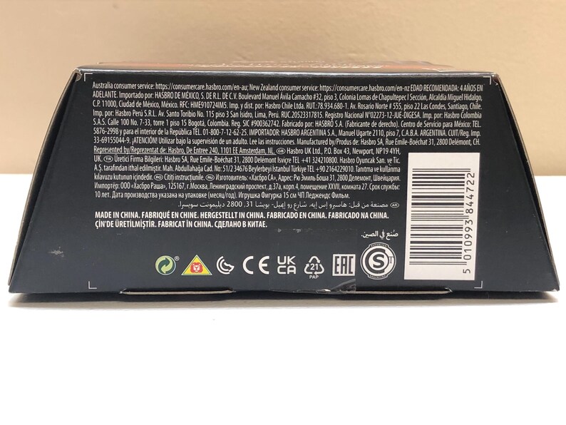 May include: Black cardboard box with a brown top flap. The box has a barcode, text in multiple languages, and several safety and certification logos, including CE, UKCA, and EAC. The text includes the words "Made in China" and "Fabricado en China".
