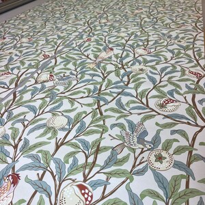 May include: A white background with a repeating pattern of stylised green leaves, brown branches, and blue birds. The pattern features pomegranates with red and white details.