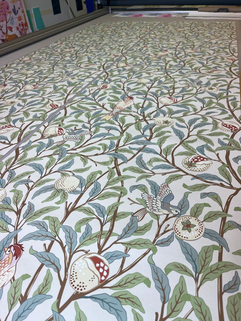 May include: A white background with a repeating pattern of stylised green leaves, brown branches, and blue birds. The pattern features pomegranates with red and white details.