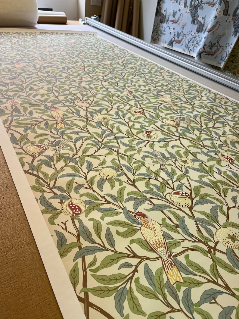 May include: A cream-coloured wallpaper with a repeating pattern of green leaves, brown branches, and yellow birds. The birds are perched on the branches and have red accents on their chests. The wallpaper has a vintage aesthetic.